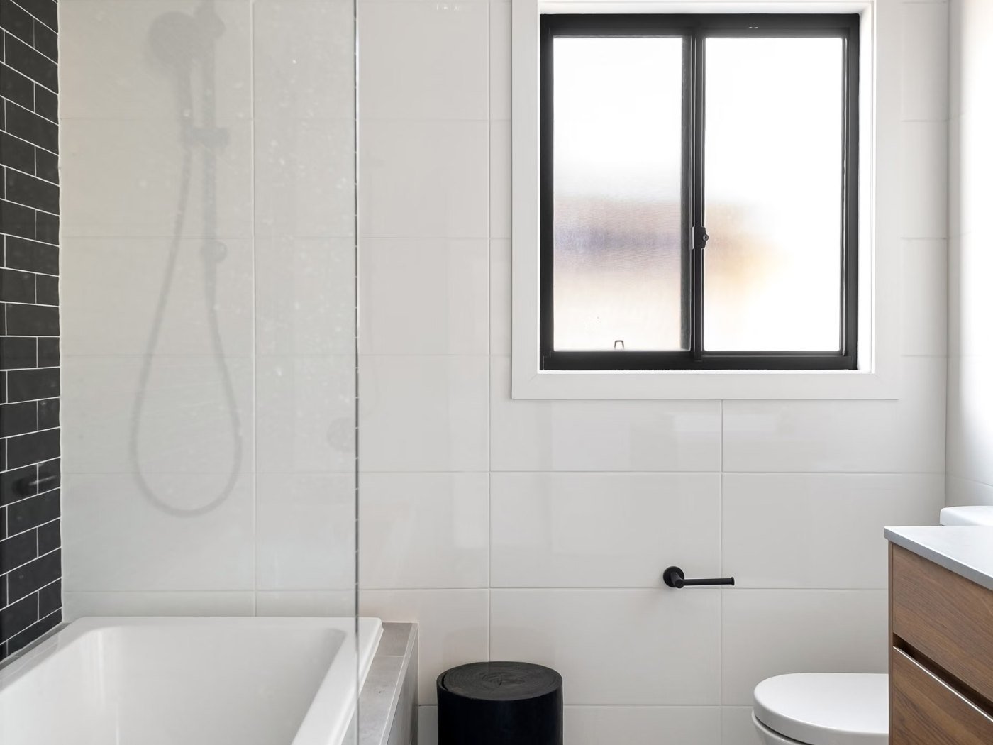 Finished bathroom addition in a Longview WA home &mdash; bath with a shower over it, an obscured-glass window, black tapware and a timber vanity
