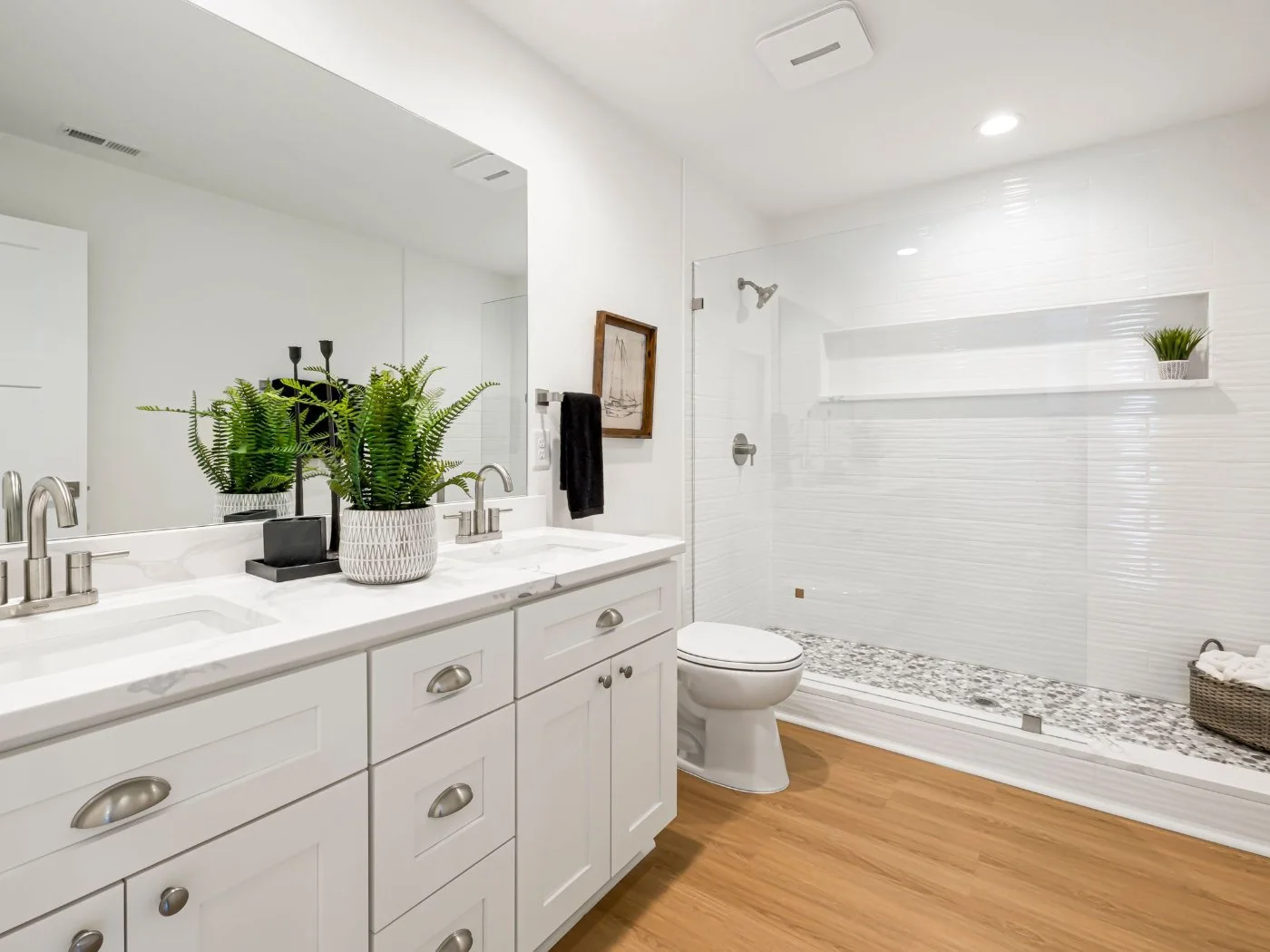 Bathroom remodeling West Side Highway — white shaker vanity with a large mirror, potted ferns and a walk-in shower tiled in white subway tile with a pebble floor