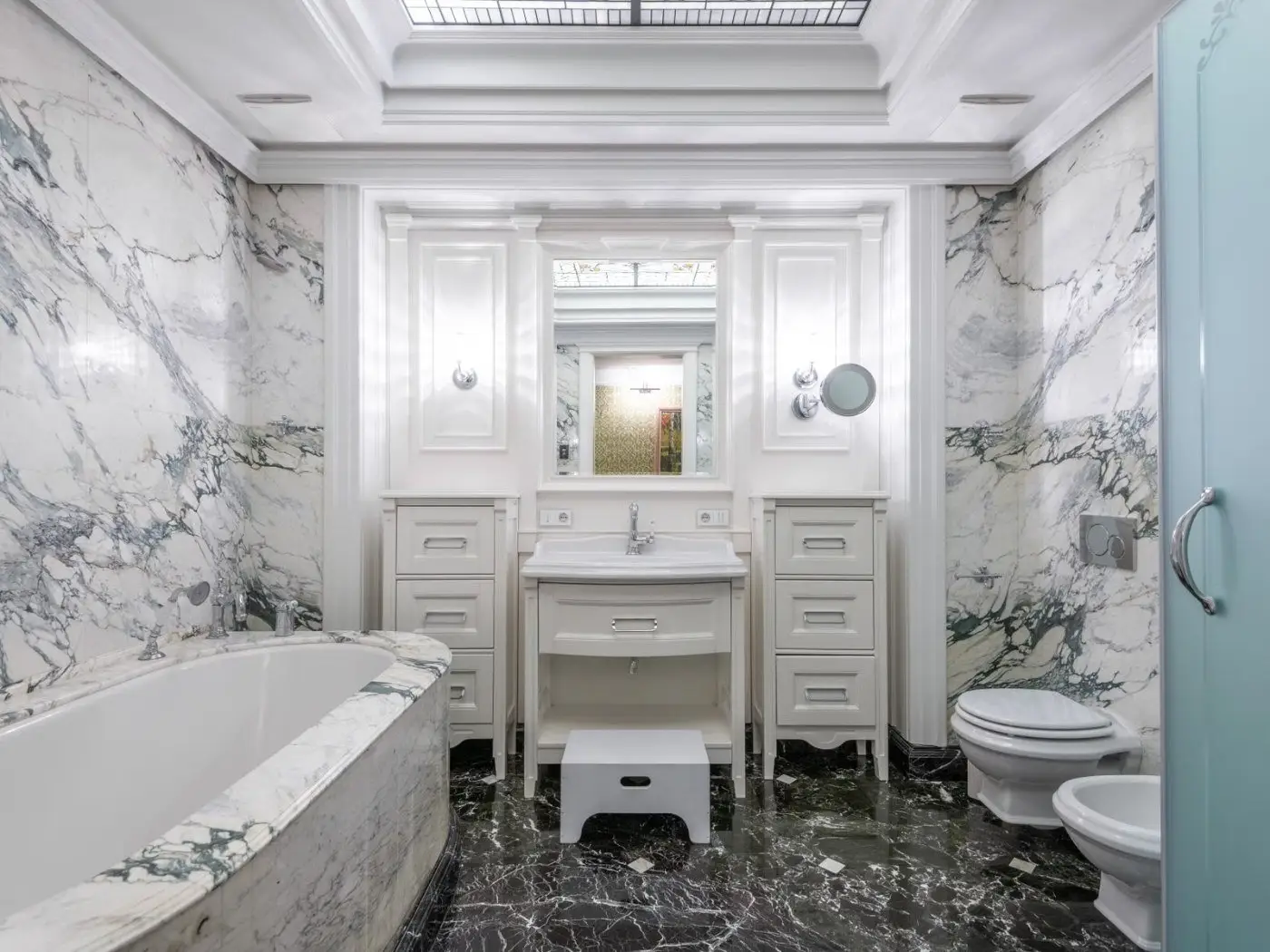 Bathroom tile contractor Longview WA work — a marble bathroom with veined white marble walls, a panelled vanity and basin, a bath to the left and a dark veined stone floor running the length of the room