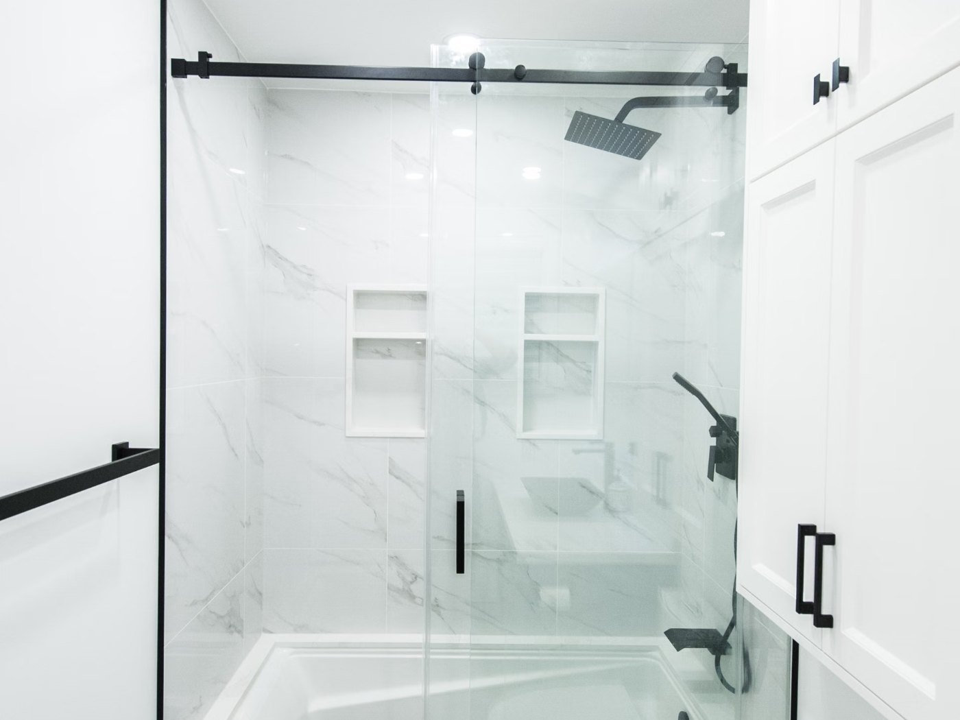 Bathroom remodeling Kelso WA — walk-in glass shower with marble tile, a black-framed sliding door and a built-in niche